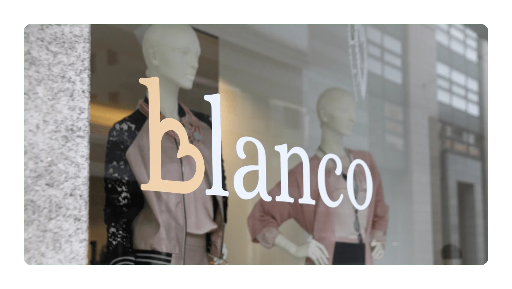 Dettaglio del logo Blanco sul vetro della boutique con manichini sullo sfondo